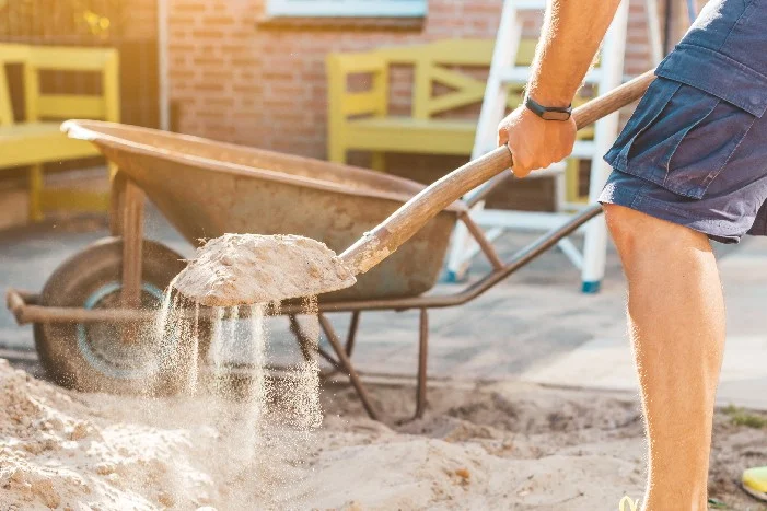 Person schaufelt Sand in Schubkarre